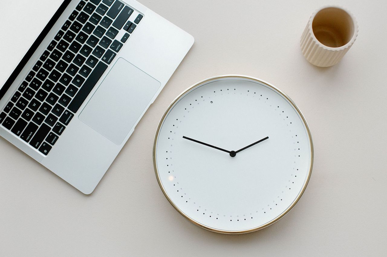 Analog clock beside a laptop